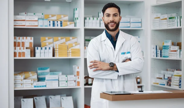 Pharmacist, man and arms crossed with medicine, portrait and confident with trust, healthcare and happiness. Face, Latino male and employee with smile, pharmacy and wellness in store and happy expert.
