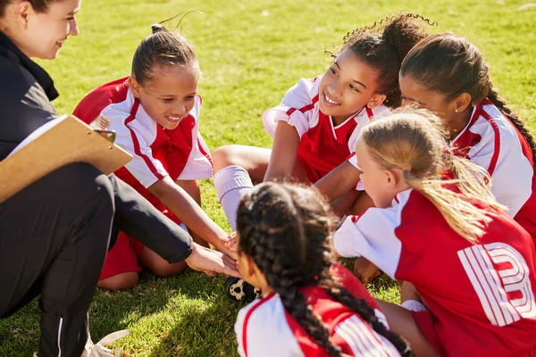 Girl soccer group, sitting and planning with coach on field with smile, team building or motivation at training. Female kids, sports diversity or happy with friends, teamwork or strategy for football.