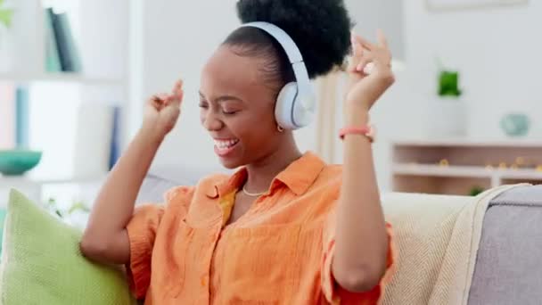 ヘッドフォンでソファで踊る黒人女性 音楽ストリーミングと精神衛生 ウェルネスと幸せなエネルギー アフリカ人はソファで踊り オーディオ技術を聞き ヒップホップオーディオを歌います — ストック動画