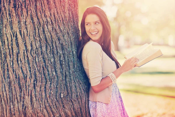 Letting my mind wander for a while. a beautiful young woman reading a book while leaning against a tree trunk