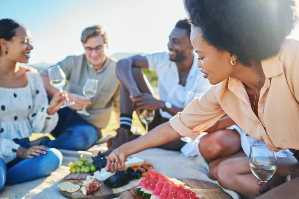 Friends, travel and picnic with food and outdoor in nature, fruit and cheese for nutrition and adventure in park. Wine, sun and summer holiday with social group, diversity and young people together
