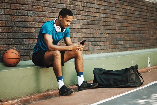 Man, basketball and phone with sports app, communication and social media online outdoor. Sport male in rest after fitness, exercise and game time check, message or text on mobile 5g smartphone.