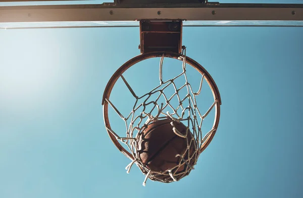 Basketball, net and ball below in sports game outdoors for sports match in the USA. Sport and airball of throw to score point for win, victory against fiberglass board with blue sky background.