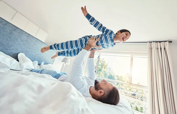 Father, son and dad playing with his child on a bed holding him having fun in a bedroom feeling happy, carefree and excited. Parent, kid and dad bonding with young boy in a house together.