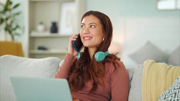 Freelance woman, phone call and laptop while headphones and talking on phone to contact for small business or online order sitting on sofa at home. Female working remote with technology in Singapore.