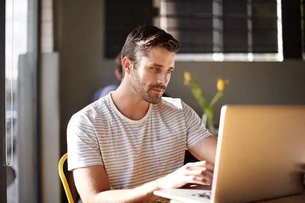 Stock image Searching for words in the afternoon sun. a young man working on a laptop in a cafe