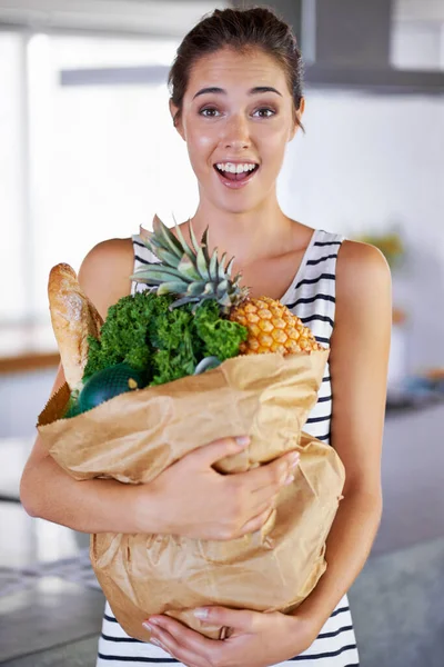Good food, great attitude. An attractive woman holding a bag of groceries in the kitchen
