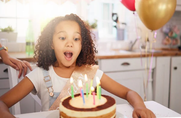 Happy birthday cake, candles and child with surprise, excited and happy face for love, care and celebration. Party, balloons and celebrate with black girl kid and dessert at the kitchen house table.