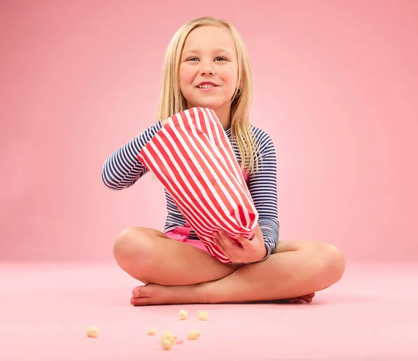 爆米花 零食和快乐的女孩在一个有粉红背景的工作室里坐着与电影零食 带着纸袋和薯片的食物 快乐和饥饿的幼儿带着微笑吃饭和感觉放松 — 图库照片