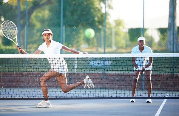 Tennis, fitness and a sports woman hitting a ball over a net during a competitive game to return a serve. Exercise, health or training with a female athlete and doubles partner playing on a court.