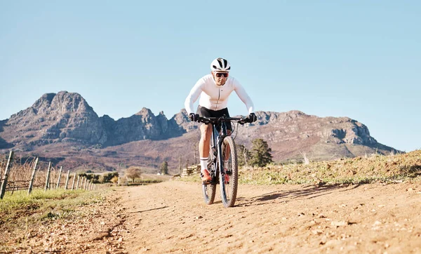 Man, mountains and cycling on trail in nature, countryside and blue sky for triathlon sports in Cape Town. Cyclist, bicycle and off road path outdoor for fitness, bike exercise and energy in sunshine.