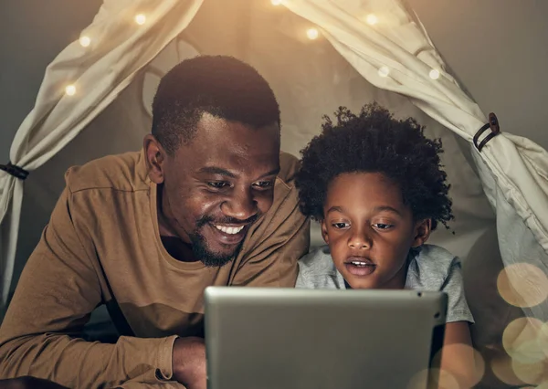 Black family, tablet and father with kid in tent at night watching movie, video and having fun in home. Technology, bokeh and smile of happy dad bonding with boy child while streaming film in house