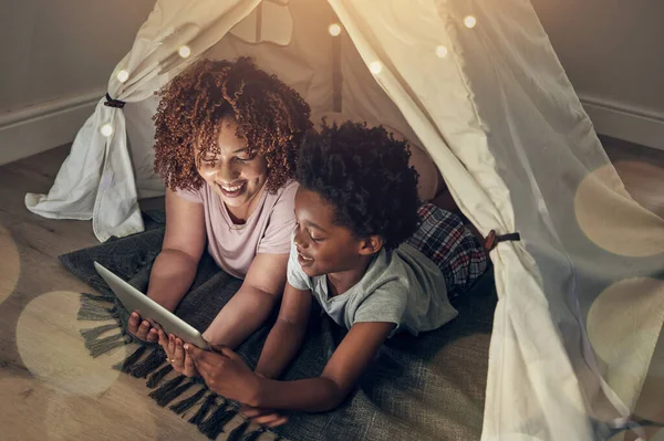 Black family, tablet and mother with kid in tent at night watching movie, video and having fun in home. Technology, bokeh and smile of happy African mom bonding with boy child while streaming film.