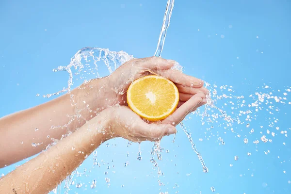 stock image Water splash, zoom or orange in hands for skincare wellness, nutrition or health in blue background studio. Water, shower or cleaning fruit in hand for natural, organic or fresh food vitamin C splash.