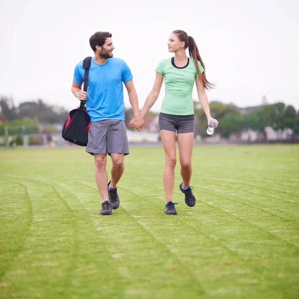 一起到田里去一对穿着运动服的年轻夫妇手牵手在运动场上散步 — 图库照片