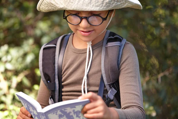 Reading and nature are his two favourite things. a young kid reading a book outdoors