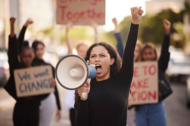 Kadın, megafon ve cemiyetteki yumruk şehirde değişimi, cinsiyet temelli şiddeti veya eşitliği protesto ediyor. Kızgın kadın eylemci, insan hakları veya hükümet hareketi için yürüyüş grevinde birlikte duruyor.