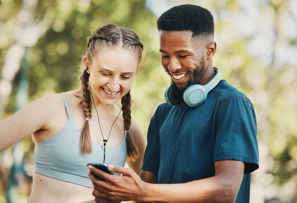 フィットネス ソーシャルメディア トレーニング モバイルアプリ 面白いビデオのための公園で電話を持つカップル コミュニケーション コメディ 黒人男性と女性は 自然の中で携帯電話で心臓のトレーニングについて読んで — ストック写真