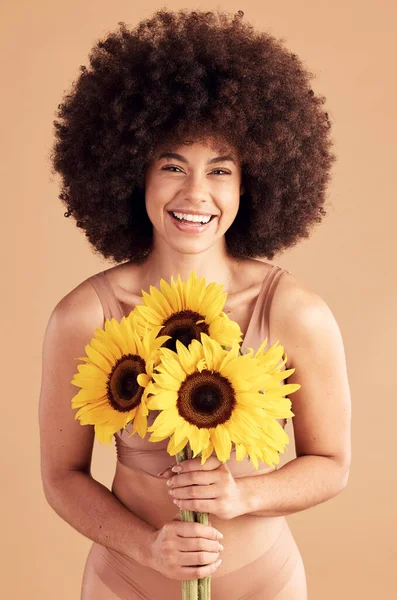 Beauty, skincare and black woman with sunflower, smile and natural hair on a studio background for cosmetics, makeup and self love. Portrait afro female with flowers for spring dermatology and glow.