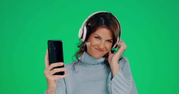 电话和耳机 在绿色工作室的背景下 听着带着微笑的音乐跳舞 快乐的女性 带着耳机和智能手机 在模拟中享受着音频音轨流或娱乐 — 图库视频影像