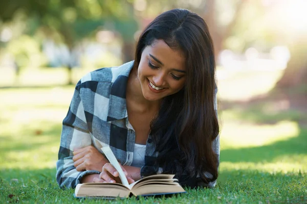 Relaxing with a good book. a young woman lying on grass and reading a book