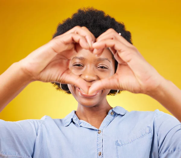 Love, heart hands sign and portrait of black woman, smile and kindness isolated on yellow background. Motivation, support and loving hand gesture, happy African model in studio with caring mindset