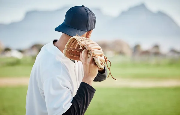 Pitcher, back view or baseball player training for a sports game on outdoor field stadium. Fitness, young softball athlete or focused man pitching or throwing a ball with glove in workout or exercise.