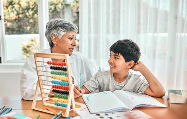 Grandma help, child abacus learning and home studying in a family house with education and knowledge. Senior woman, boy and teaching of a elderly person with a kid doing writing for a class project.