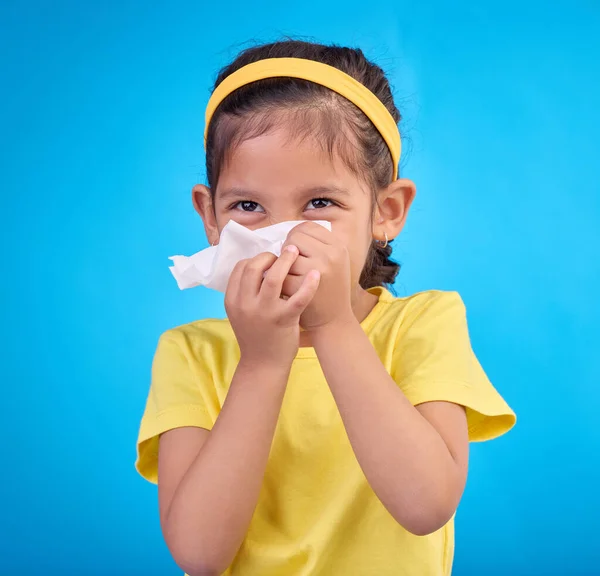 Sick, blowing nose and napkin with girl in studio for allergies, illness and sneezing. Hay fever, bacteria and sinus issue with child and tissue isolated on blue background for health, medical or flu.