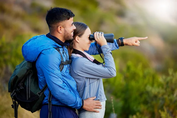 stock image Binoculars, point and a couple bird watching in nature while hiking in the mountains together. Forest, ecology or sightseeing with a man and woman looking at the view while bonding on a hike.