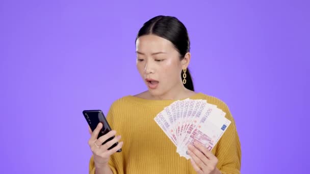 スタジオで電話 お金とショックを受けたアジアの女性 紫の背景に隔離された幸せな勝利のお祝い 現金獲得 オンラインソーシャルメディアのプロモーションや競争上の興奮の影響力とボーナス賞 — ストック動画