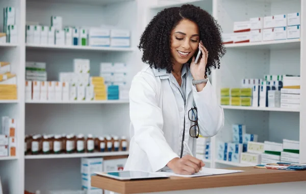 stock image Phone call, counter and pharmacist woman for medicine note, customer service or virtual healthcare support. Happy, friendly doctor, medical retail person in pharmacy talking on cellphone at help desk.