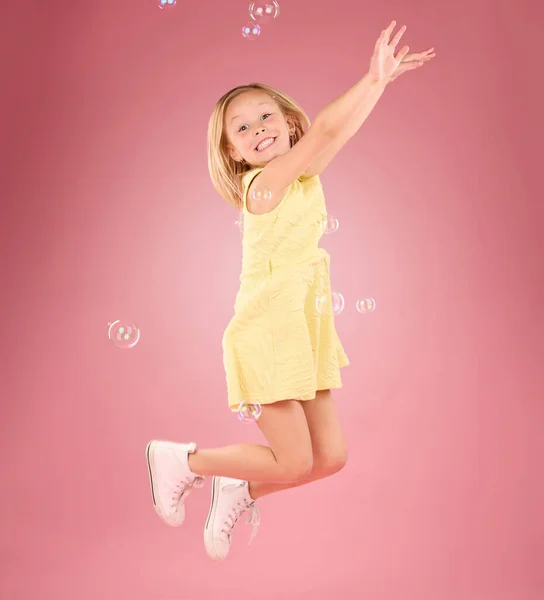Child, jump and bubbles for a smile portrait in studio with a pink background for fun. Female kid model jumping with happiness, play and cheerful face isolated on gradient color and space.