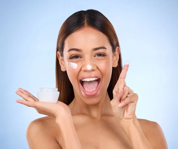 Skincare portrait of excited woman, cream on finger and anti aging skin care on blue background. Cosmetics, facial and face of hispanic model with moisturizer solution or collagen product in studio