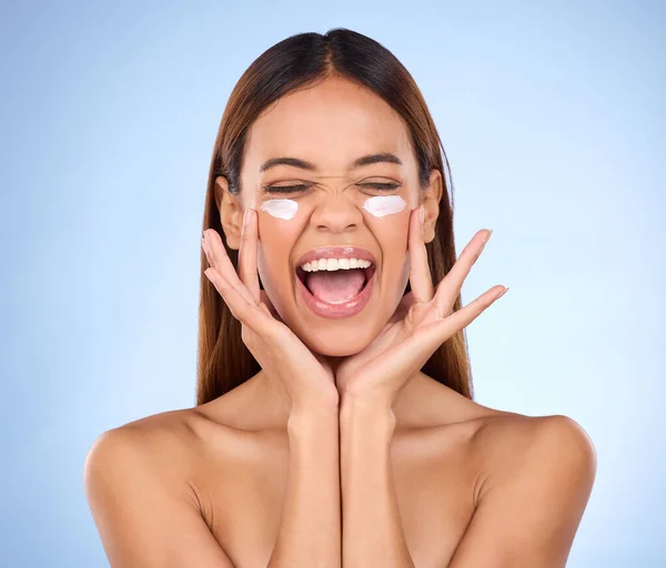 Dermatology, portrait of excited woman with cream on face and anti aging skin care on blue background. Cosmetics, facial and happy hispanic model, moisturizer solution or collagen product in studio