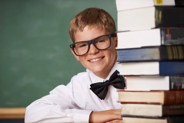 This is any bookworms dream. A young boy wearing glasses and a bow-tie smiling at the camera from behind a stack of books