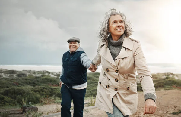 Beach, love and senior couple holding hands on romantic evening walk in nature on happy date. Smile, romance and retirement, old woman and man walking on ocean path at sunset on holiday in Australia