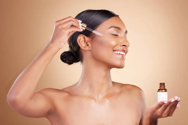 stock image Woman, dropper and retinol on face for skincare beauty or cosmetics against a studio background. Happy female model with smile applying oil drop to skin for hydration, moisturizer or facial treatment.