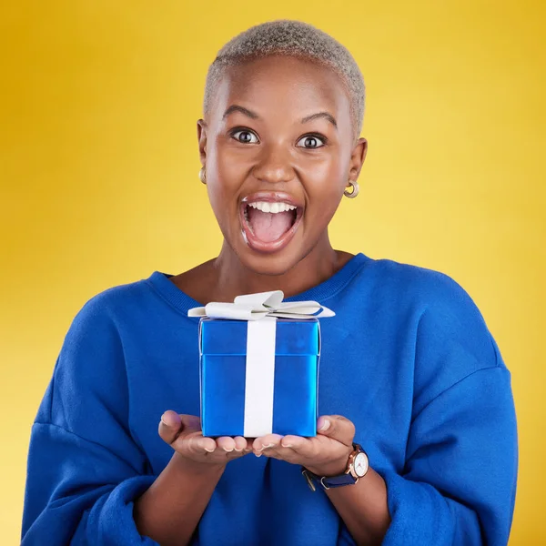 Excited, portrait and black woman with birthday gift in studio isolated on a yellow background. Face, box and happy African female with present for celebration, party and holiday for special event