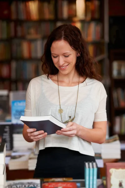 Judging a book by its back cover. A young woman reading the back cover of a novel while browsing in a bookshop