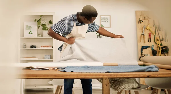 African american tailor looking at his material. Young fashion designer checking a roll of fabric. Creative entrepreneur looking at textiles in his studio. Small business owner working on designs.