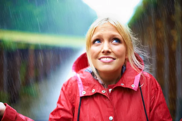 Its started raining. Gorgeous young blonde woman wearing a red raincoat in the rain outdoors on a country road