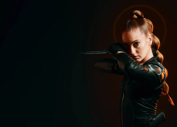 Woman, warrior and knife in studio with space for action, fight and safety from danger. Strong female model, assassin or agent in scifi leather cosplay costume with weapon on a dark mockup background.