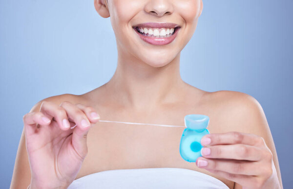 Closeup of a smiling mixed race young woman with glowing skin posing against blue copyspace background while flossing her teeth for fresh breath. Hispanic model using floss to prevent a cavity.