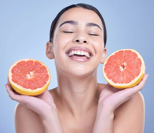 A happy mixed race woman holding a grapefruit. Hispanic model promoting the skin benefits of citrus diet against a blue copyspace background.