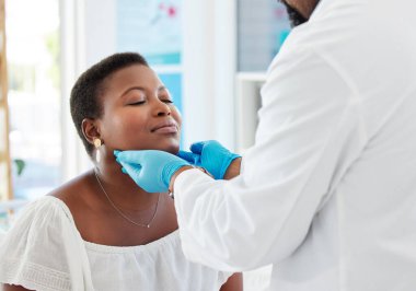 Boğazı ağrıyan Afrikalı Amerikalı kadın konsültasyonda. Doktor hasta bir hastanın boğazını kontrol ediyor. Muayene sırasında bir hastanın boynunu muayene eden bir tıp uzmanı.