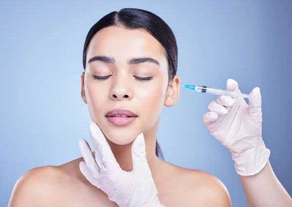 A gorgeous mixed race woman getting botox filler in her face. Hispanic model getting cosmetic surgery against a blue copyspace background.