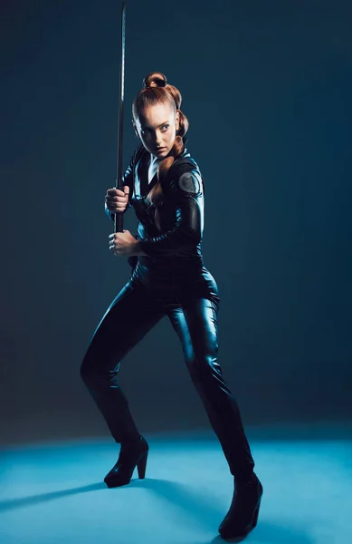 Woman, warrior and vigilante in cosplay with sword stance for battle, war or game against dark studio background. Female in black widow costume standing ready with blade for halloween or hunger games.