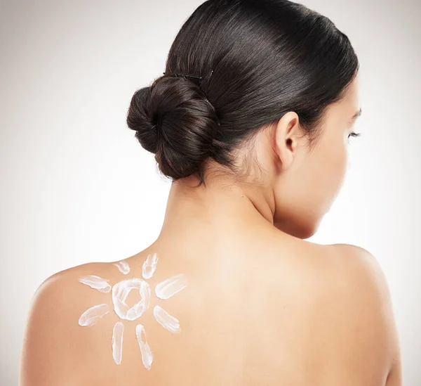 stock image Back of a beautiful woman showing her applying cream on her shoulder posing against a grey studio background. Skincare is important. Protection from the sun.