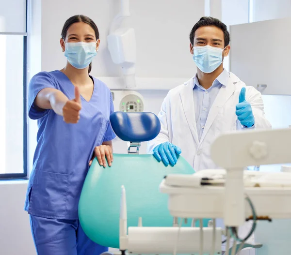 以前よりも明るい笑顔をお届けします 診察室に親指を立てた二人の若い歯科医の肖像画 — ストック写真